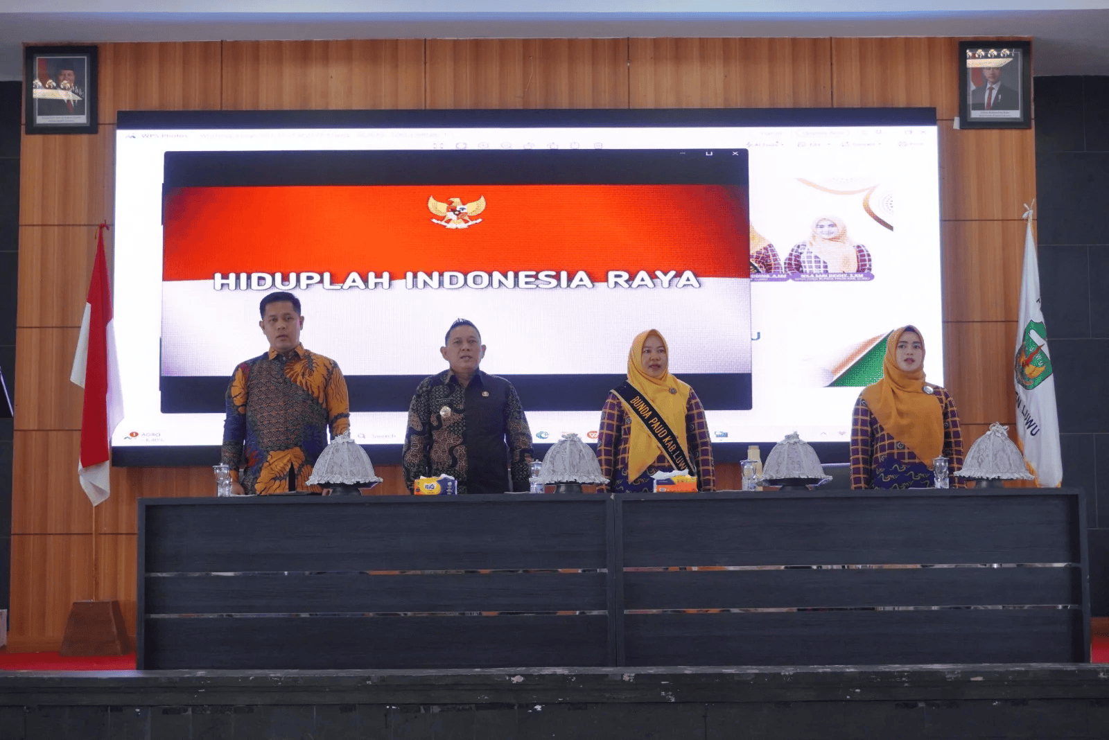 Pelaksanaan upacara bendera di ruang auditorium, menampilkan pejabat dan peserta berseragam batik, menyampaikan semangat nasionalisme Indonesia.