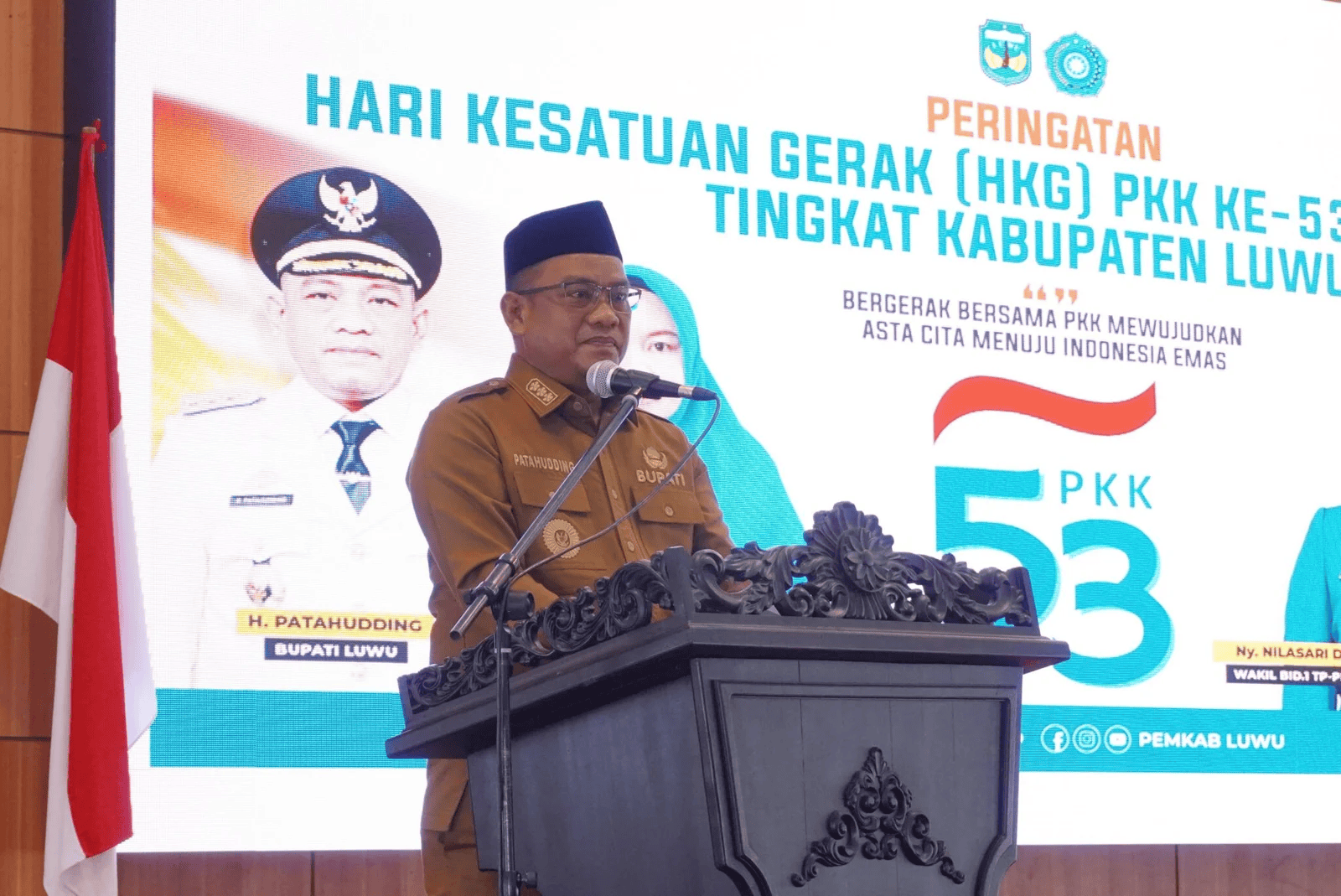 Laki-laki berpakaian seragam pemerintahan berbicara di depan podium dengan latar belakang poster acara HKG PKK.
