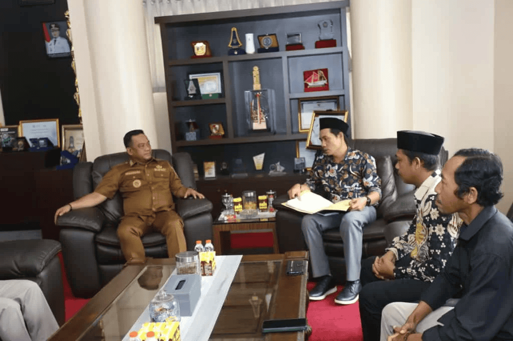 Perwakilan pemerintah dan masyarakat berdiskusi serius di ruang pertemuan kantor.